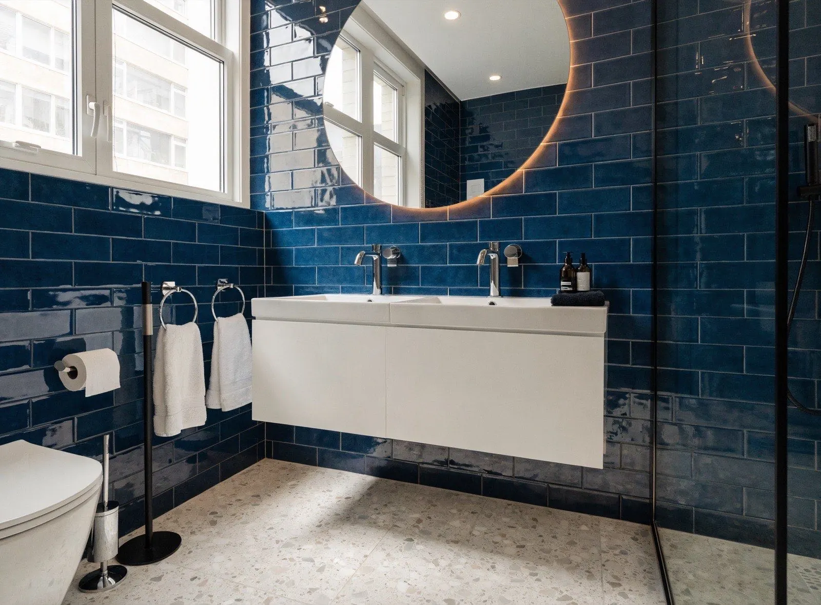 Salle de bain rénovée avec carrelage bleu marine, double vasque et miroir rétroéclairé